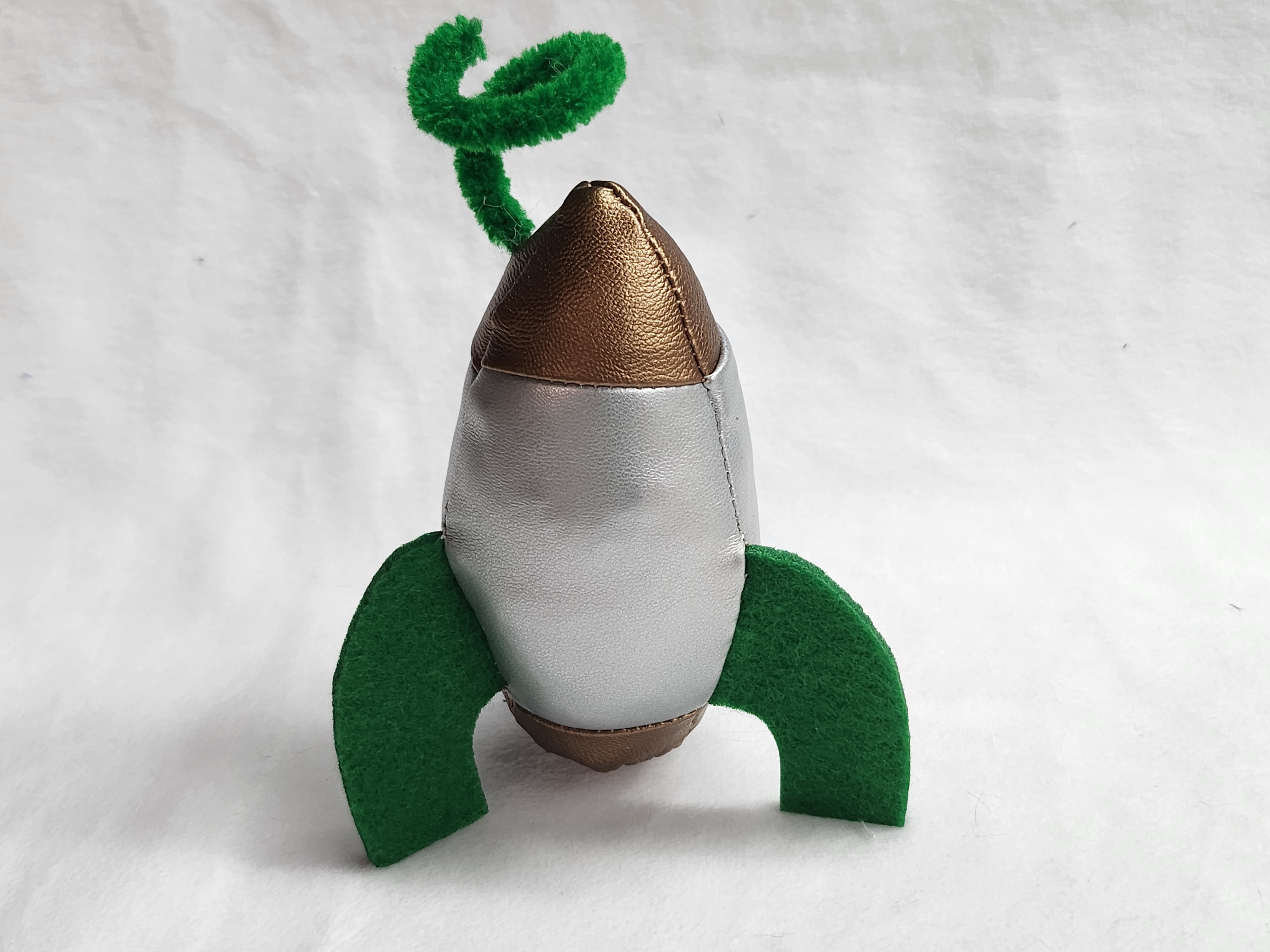 A small silver rocket with copper nosecone and tail, green fins, and a fuzzy green antenna.