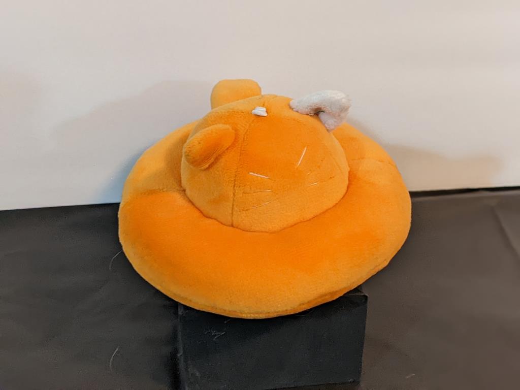 A flying saucer with cat ears, a tail, and whiskers. It is orange with one white ear.